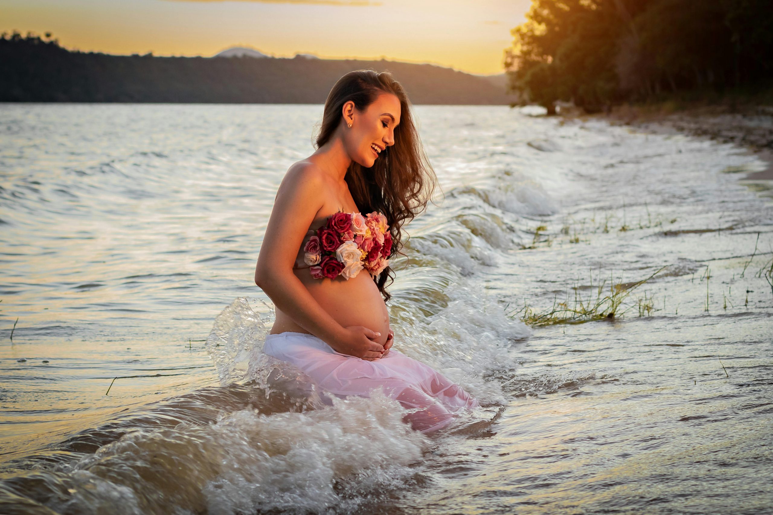 pregnant woman sitting on the shoreline as waves roll in