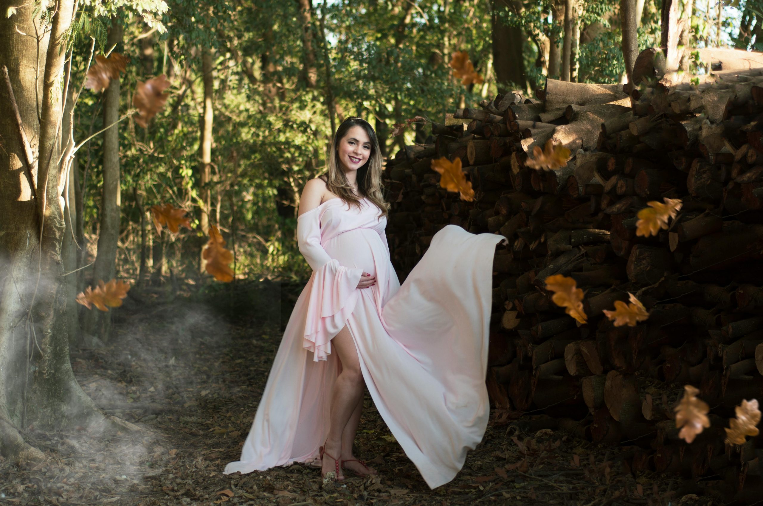 pregnant woman in a pink flowing dress posing while leaves fall