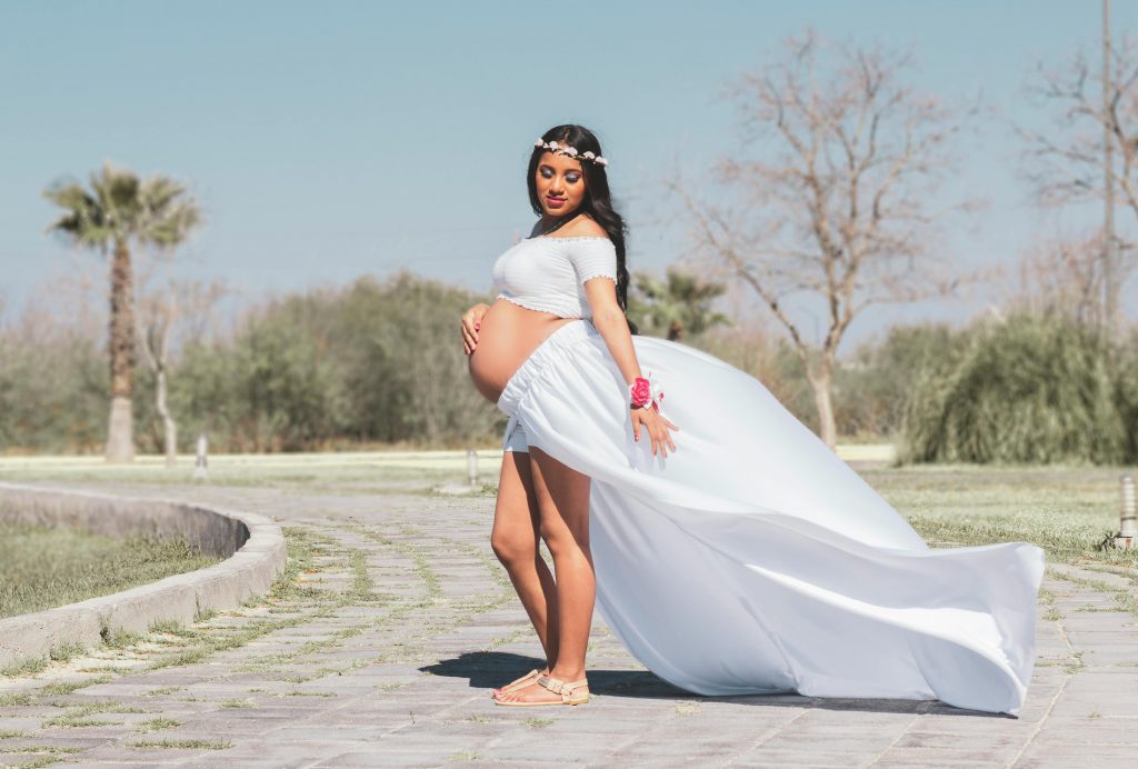 pregnant woman in a flower crown, and flowing white outfit, posing outdoors