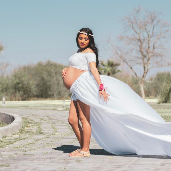 pregnant woman in a flower crown, and flowing white outfit, posing outdoors